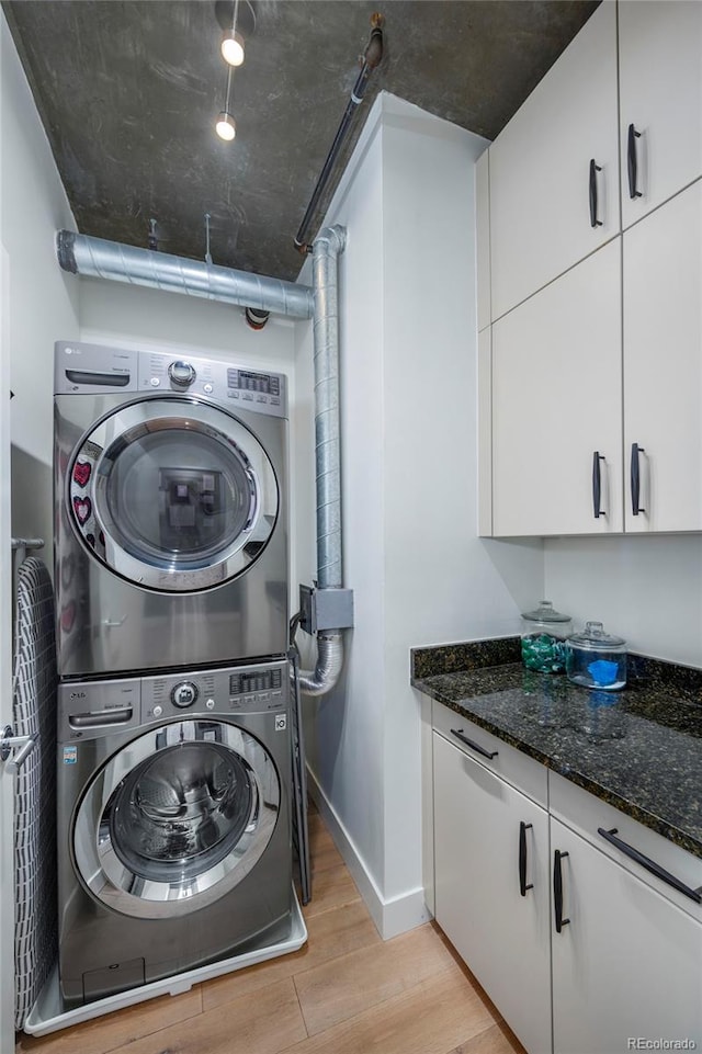 clothes washing area with cabinets, stacked washer and dryer, and light hardwood / wood-style flooring