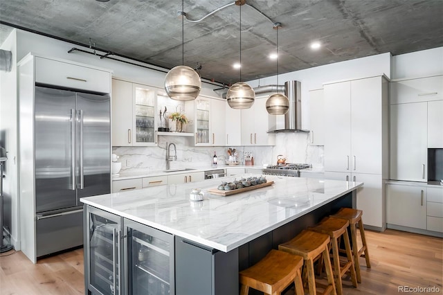 kitchen with pendant lighting, a center island, wall chimney range hood, wine cooler, and built in refrigerator