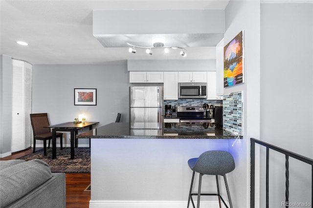 kitchen featuring kitchen peninsula, dark stone countertops, appliances with stainless steel finishes, tasteful backsplash, and white cabinetry