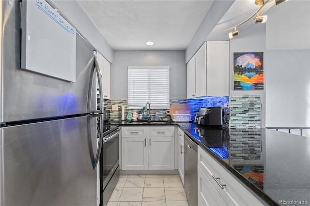 kitchen with white cabinetry, sink, stainless steel appliances, backsplash, and dark stone countertops