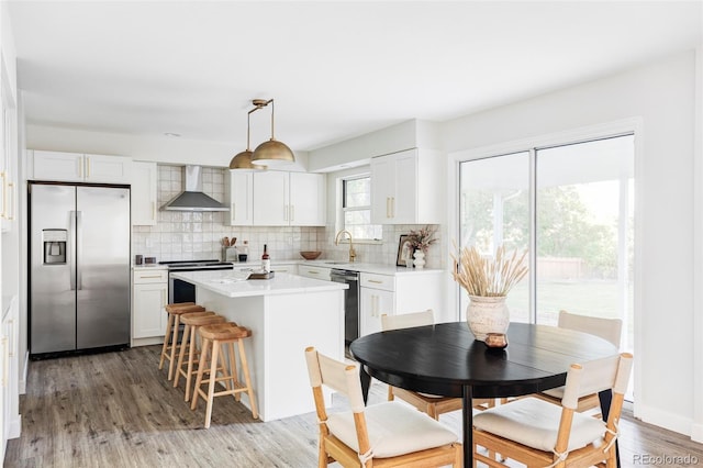 kitchen featuring stainless steel appliances, wall chimney range hood, and white cabinets