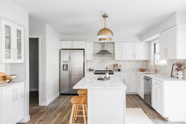 kitchen with sink, hanging light fixtures, a kitchen island, wall chimney range hood, and appliances with stainless steel finishes