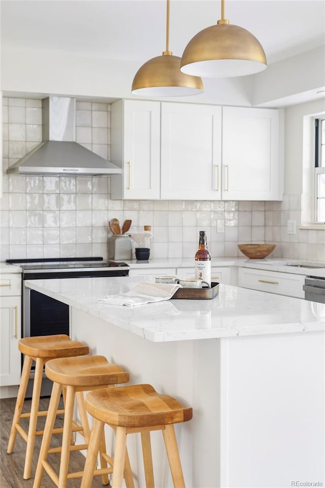 kitchen featuring wall chimney range hood, decorative backsplash, and a breakfast bar area