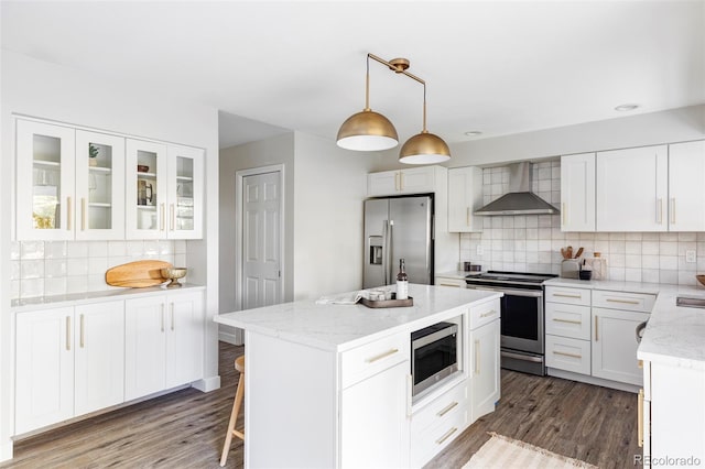 kitchen featuring appliances with stainless steel finishes, wall chimney range hood, pendant lighting, and white cabinetry