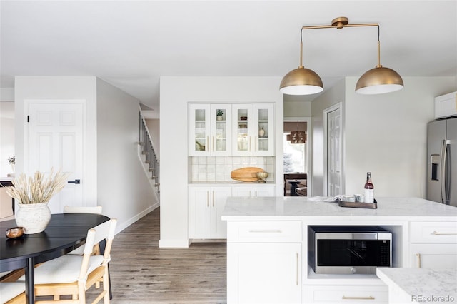 kitchen featuring white cabinets, pendant lighting, light stone counters, and appliances with stainless steel finishes