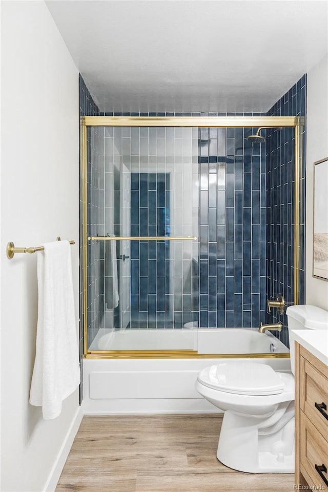 full bathroom with combined bath / shower with glass door, hardwood / wood-style floors, vanity, and toilet