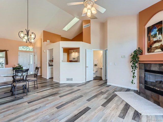 living room featuring high vaulted ceiling, a tile fireplace, ceiling fan with notable chandelier, a skylight, and hardwood / wood-style flooring