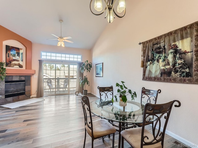 dining area with hardwood / wood-style flooring, ceiling fan, a fireplace, and a high ceiling