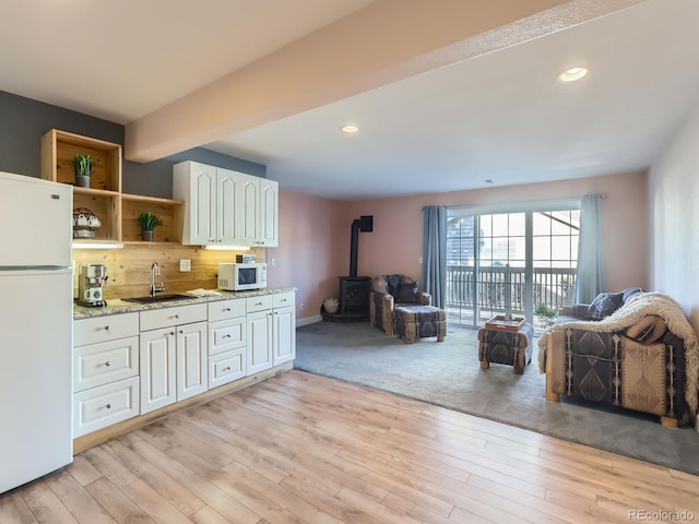 kitchen with light hardwood / wood-style floors, white appliances, sink, and a wood stove