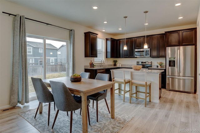 kitchen featuring stainless steel appliances, dark brown cabinets, hanging light fixtures, light wood-type flooring, and a center island