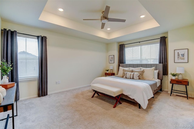 bedroom featuring light colored carpet, a tray ceiling, and multiple windows