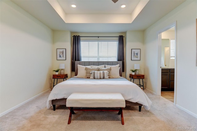 bedroom with ensuite bath, baseboards, a tray ceiling, and light colored carpet