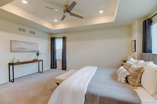 bedroom with light colored carpet, a raised ceiling, and visible vents