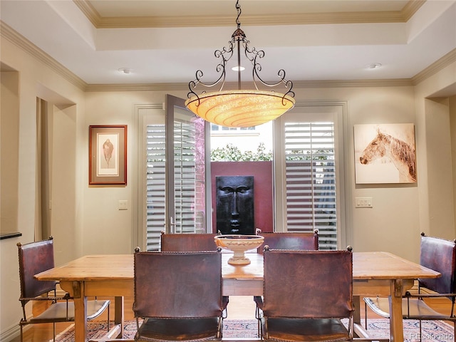 dining area with wood finished floors, a raised ceiling, an inviting chandelier, and ornamental molding