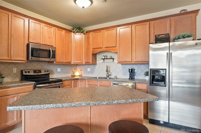 kitchen with appliances with stainless steel finishes, light tile patterned floors, decorative backsplash, sink, and a breakfast bar area