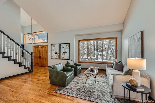 living area with light wood finished floors, a towering ceiling, a chandelier, baseboards, and stairs