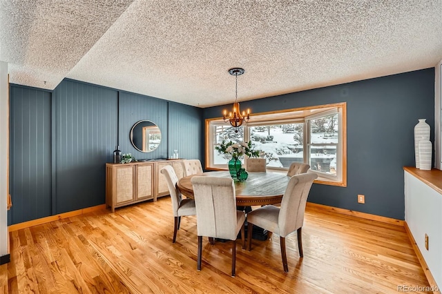 dining space featuring a notable chandelier, a textured ceiling, baseboards, and wood finished floors