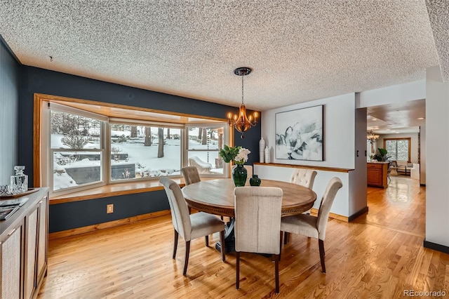 dining room featuring baseboards, light wood-style flooring, a chandelier, and a textured ceiling