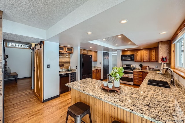 kitchen with a peninsula, a sink, a kitchen bar, black appliances, and a raised ceiling