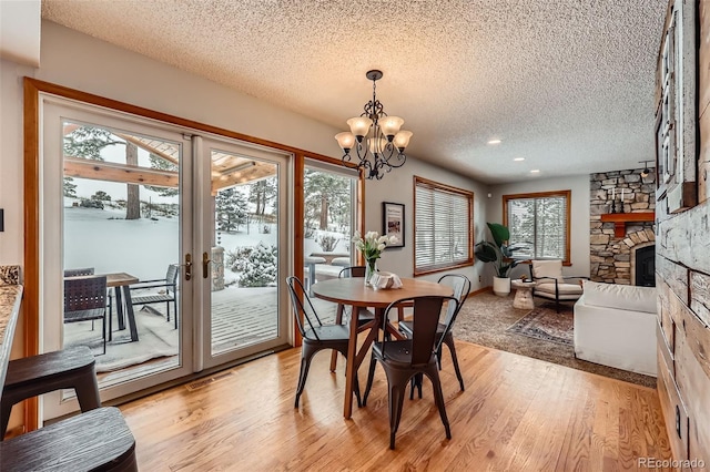 dining space featuring a stone fireplace, plenty of natural light, light wood-style flooring, and a textured ceiling