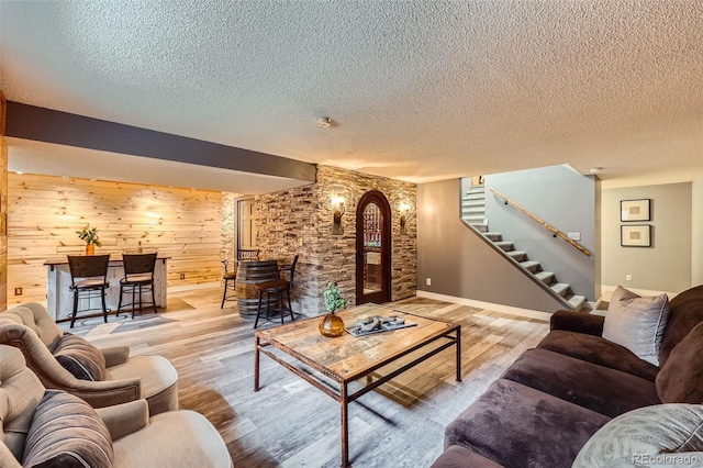 living room featuring a textured ceiling, light wood-style flooring, wood walls, baseboards, and stairs