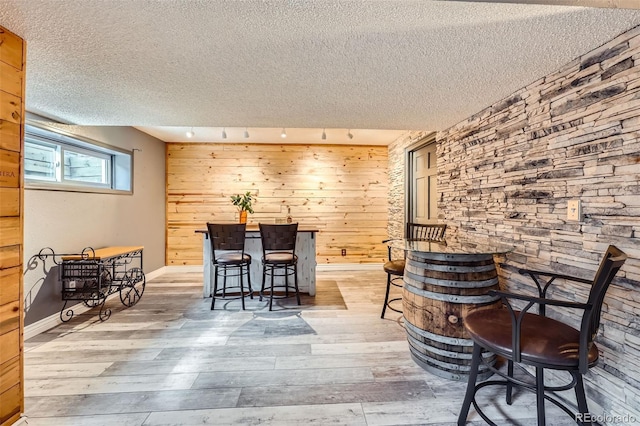 dining area with a textured ceiling, wood walls, light wood-type flooring, and baseboards