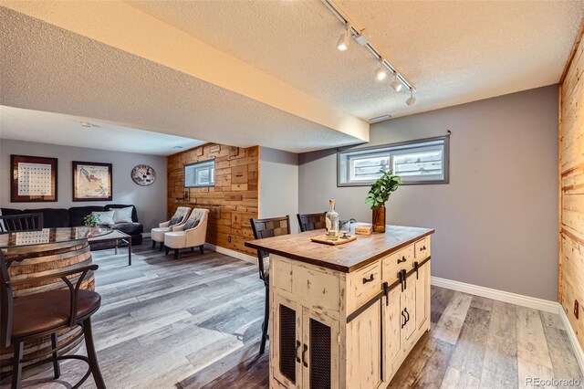 interior space with open floor plan, wood finished floors, a center island, a textured ceiling, and wood walls