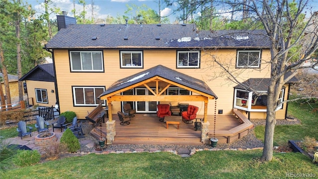 rear view of property featuring a yard, a chimney, a fire pit, and a wooden deck