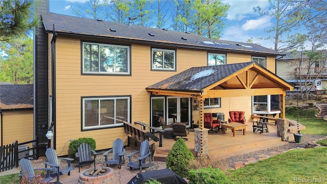 back of property with an outdoor fire pit, a chimney, roof with shingles, and a deck