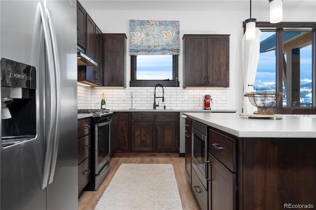 kitchen featuring appliances with stainless steel finishes, sink, backsplash, and decorative light fixtures