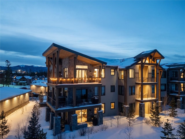 snow covered back of property with a mountain view and a balcony