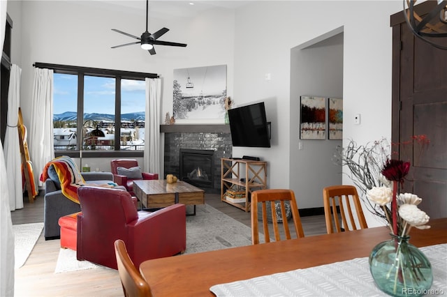 living room featuring a high ceiling, ceiling fan, a stone fireplace, and light wood-type flooring