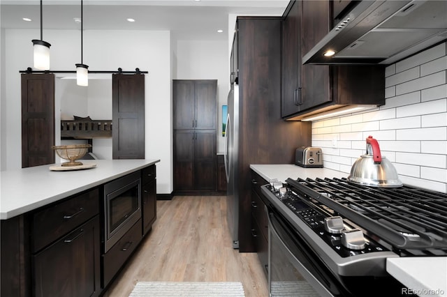 kitchen with hanging light fixtures, range hood, gas range oven, built in microwave, and a barn door