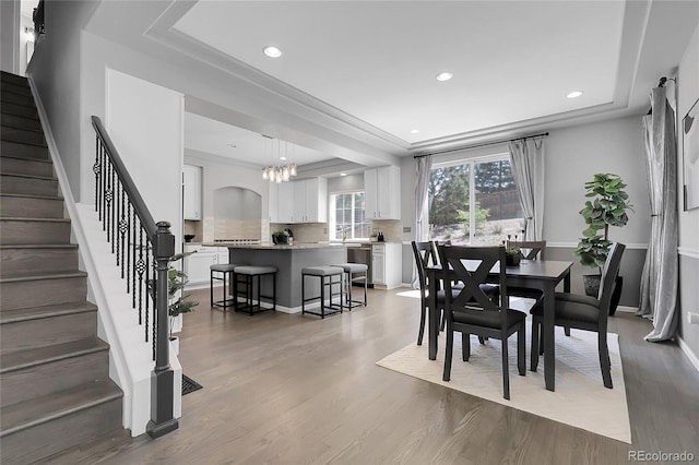 dining space featuring a raised ceiling, stairway, recessed lighting, light wood-style floors, and a chandelier