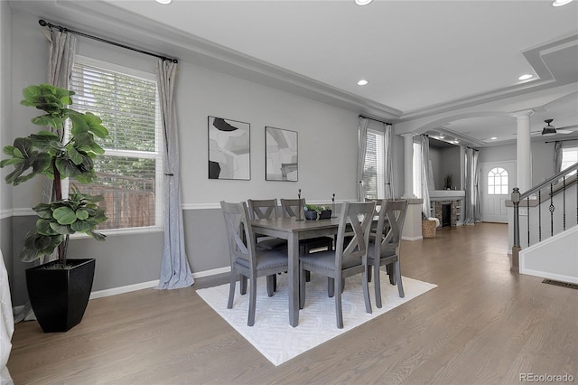 dining space with ornate columns, light wood-type flooring, recessed lighting, a fireplace, and arched walkways
