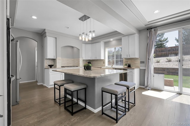 kitchen with a kitchen bar, arched walkways, dark wood finished floors, tasteful backsplash, and recessed lighting
