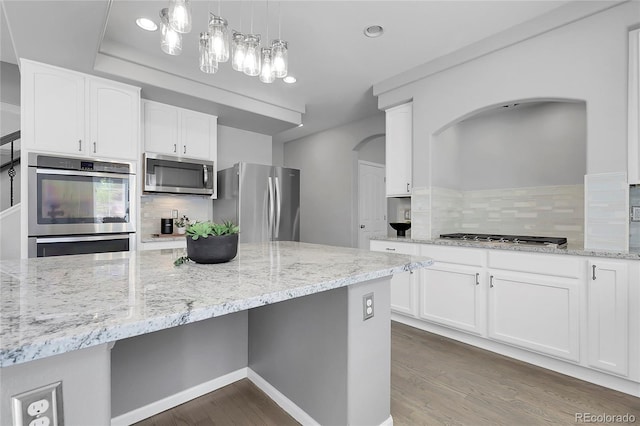 kitchen with appliances with stainless steel finishes, dark wood finished floors, decorative backsplash, arched walkways, and recessed lighting