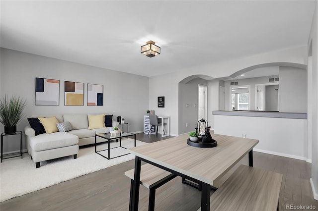dining space with arched walkways, wood finished floors, and baseboards