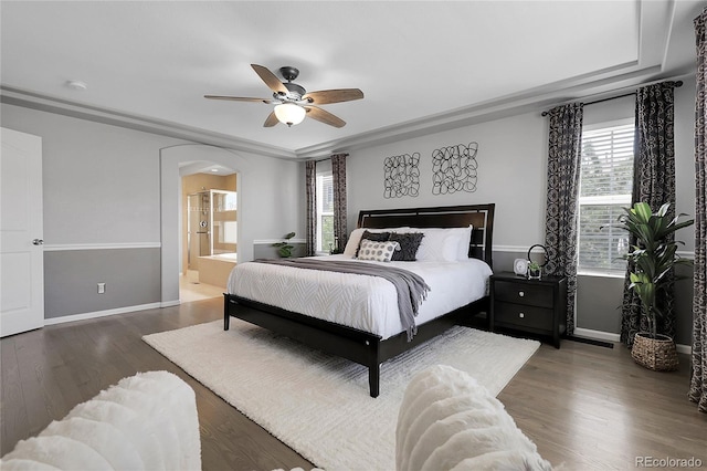 bedroom with baseboards, arched walkways, wood finished floors, and ensuite bathroom