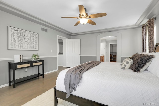 bedroom with arched walkways, wood finished floors, baseboards, and a spacious closet