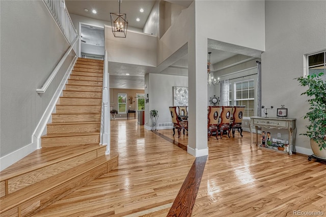 entrance foyer featuring a chandelier, light wood-type flooring, stairs, baseboards, and a high ceiling