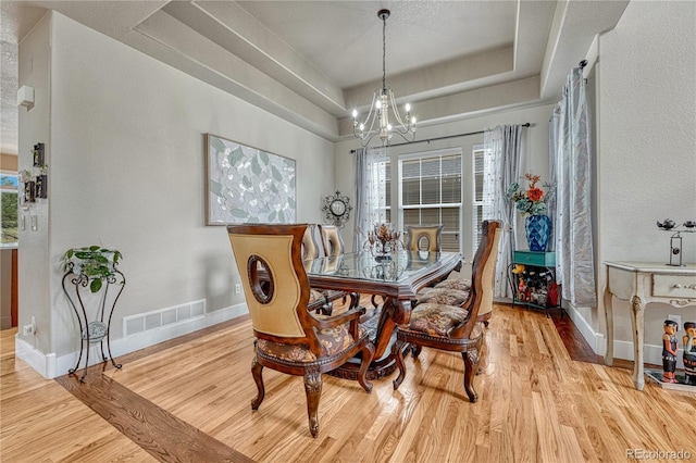 dining area featuring a chandelier, baseboards, a raised ceiling, and wood finished floors