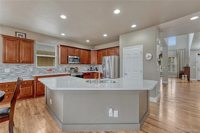kitchen featuring appliances with stainless steel finishes, a sink, a spacious island, light wood finished floors, and recessed lighting