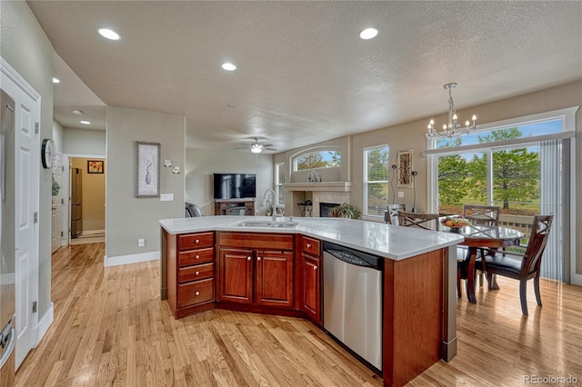 kitchen with a sink, stainless steel dishwasher, open floor plan, a fireplace, and light wood-type flooring
