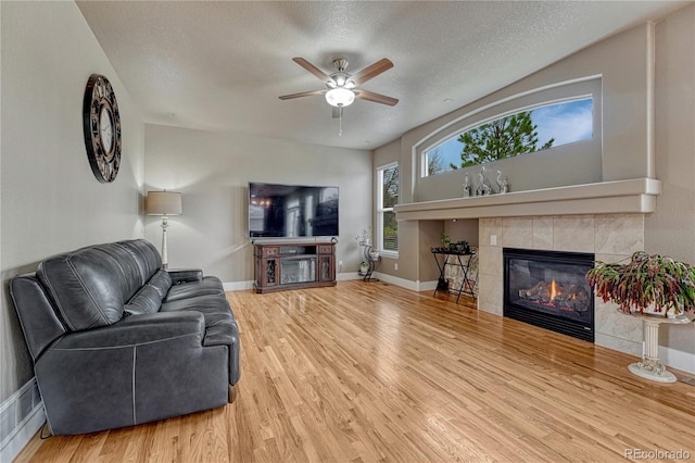 living area featuring a fireplace, ceiling fan, wood finished floors, a textured ceiling, and baseboards