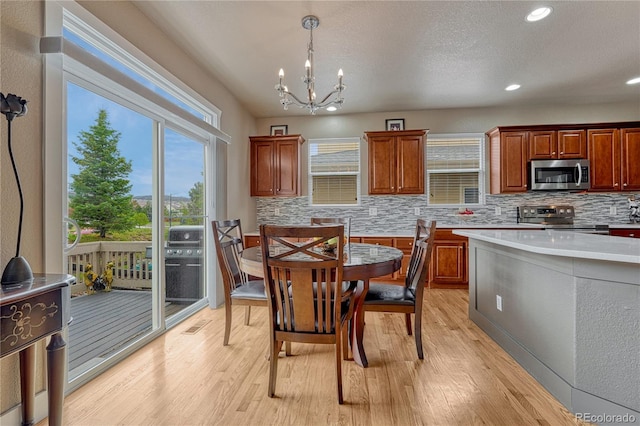 kitchen featuring stainless steel appliances, backsplash, a chandelier, light wood-style flooring, and light countertops