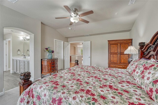 bedroom with a sink, vaulted ceiling, arched walkways, light wood-style flooring, and a ceiling fan