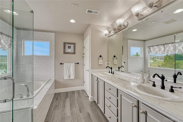 full bathroom featuring healthy amount of natural light, double vanity, a relaxing tiled tub, a textured ceiling, and a shower with shower door