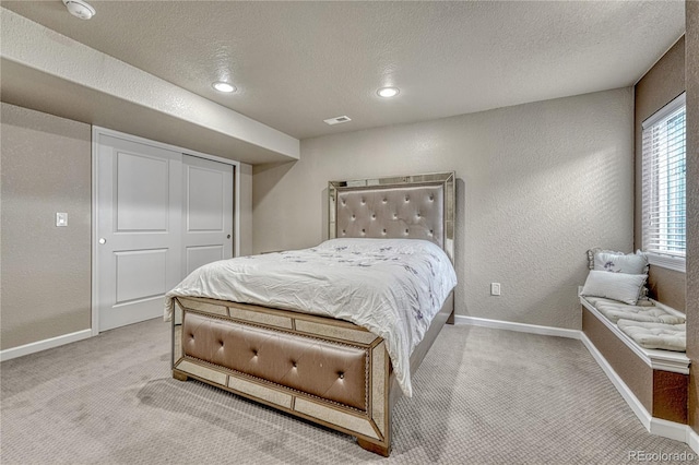 bedroom with baseboards, light colored carpet, a textured wall, a textured ceiling, and a closet