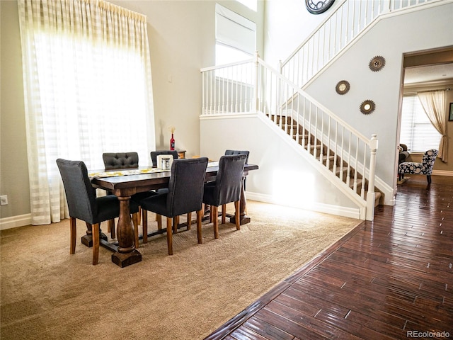 dining room with dark wood-style floors, a towering ceiling, baseboards, and stairs